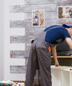 Furniture assembly worker standing reading instruction and using a tape measure. Worker tools.