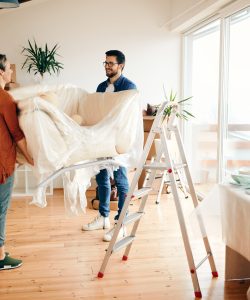 Happy couple relocating in a new home and carrying sofa in the living room.